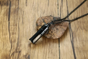 Détail du pendentif capsule noire avec centre en verre sur fond de bois et pierre