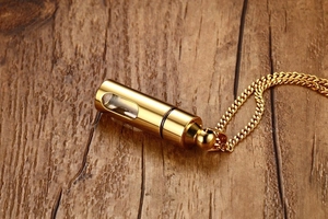 Gros plan d'un pendentif flacon de parfum cylindrique doré sur fond de bois sombre