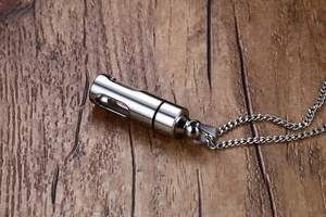Gros plan du collier capsule argenté sur une table en bois foncé avec texture