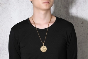 Detail of a men's gold anchor medallion necklace on a black crew neck shirt