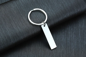 Close-up of polished stainless steel rectangular pendant and key ring on black background