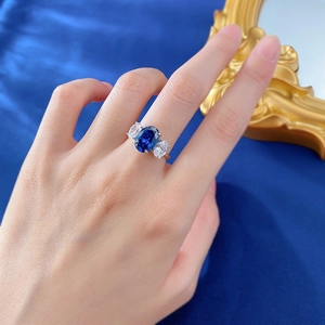 Royal blue oval gemstone ring with white side diamonds on hand over velvet background