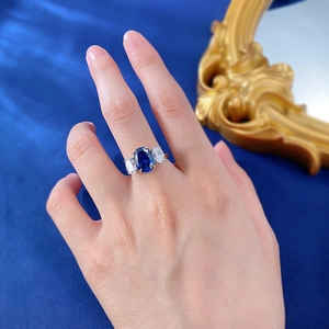 Detailed view of Royal Blue oval sapphire ring with three-stone setting on finger
