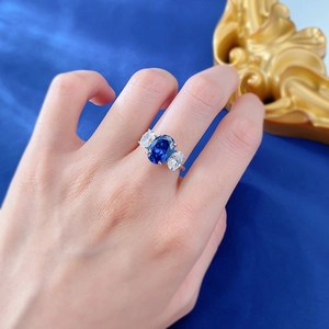 Macro detail of royal blue oval gemstone ring with three-stone setting on finger