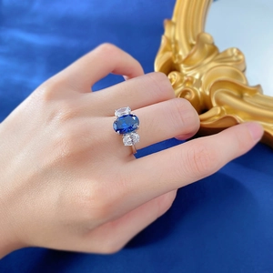 Macro shot of elegant royal blue oval sapphire ring with side diamonds on blue velvet