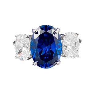 Royal blue oval sapphire three-stone engagement ring with silver prongs in white background