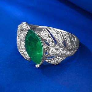 Macro detail of leaf-shaped green emerald ring with silver feather wing band