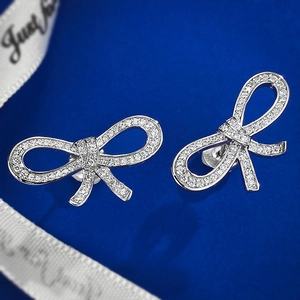 Silver bow stud earrings with sparkling pavé zircons on a dark blue textured background
