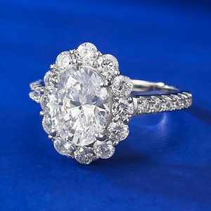 Macro shot of oval cut diamond ring with halo pavé setting on blue textured surface
