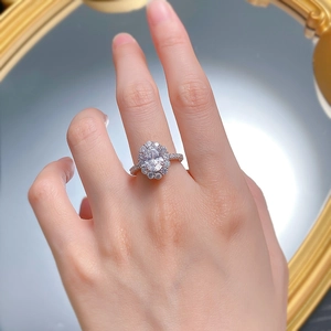 Close-up of a silver halo ring with oval-cut diamond on hand against a vintage mirror