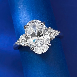Macro di un anello con diamante ovale e pietre laterali a grappolo su fondo blu