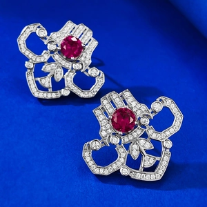 Macro shot of silver stud earrings with round red rubies and geometric halo of white gems