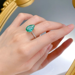 Vue macro d'une bague goutte vert émeraude portée sur la main devant un miroir rétro