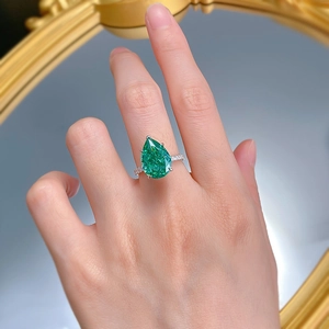 Gros plan d'une bague en émeraude taille poire avec diamants pavés sur un miroir