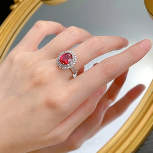 Detailed view of an oval ruby-style ring with double halo diamond setting on a finger