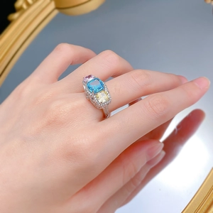 Three-stone ring featuring radiant cut pink, blue, and yellow gems on model's finger