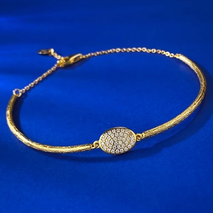 Bohemian style brushed gold bracelet with oval pavé zircon center on blue background