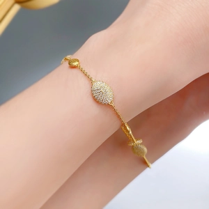 Gros plan sur bracelet doré avec disque en métal brossé et pendentif ovale pavé de diamants