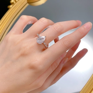 Close-up of a pear-cut teardrop diamond ring on a hand with a reflective mirror background