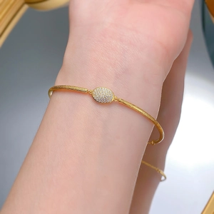 Close-up of golden brushed metal bracelet with oval diamond-studded centerpiece on wrist