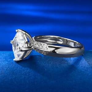 Macro side view of a radiant cut solitaire ring with micro-paved silver band on blue silk