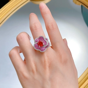 Detail view of a floral silver ring with red stone petals worn on a model's hand