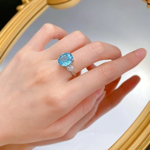 Detail of oval blue gemstone ring with heart-shaped side stones worn on finger
