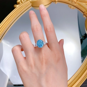 Detailed view of an oval blue gemstone ring with side stones worn on a finger