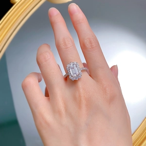 Detailed close-up of emerald cut silver ring with halo diamonds on a hand model