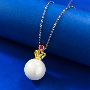Macro detail of 11mm pearl pendant with gold crown setting and red gemstone accent