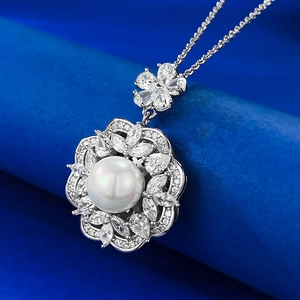Macro shot of 8mm pearl pendant necklace with zircon floral accents on blue backdrop