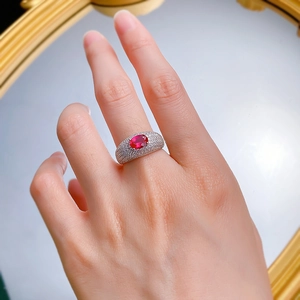Detailed view of an oval red ruby ring with pavé-set zircons worn on a finger