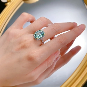 Macro shot of an emerald cut green gemstone ring with halo diamond setting on a finger