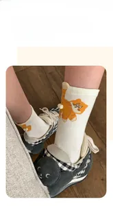 Detail of white cotton sock featuring orange cat pattern and 3D plush ball tail decoration