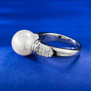Macro shot of 10mm white pearl ring with pave set stones on a blue textured surface