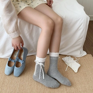 Detail of light grey knit crew socks with white polka dots, lace trim, and ribbon bows