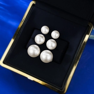 Three pairs of round white pearl stud earrings in varied sizes on black velvet display