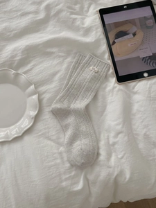 Detailansicht hellgrauer gerippter Baumwollsocken mit weißem Markenlabel auf weißem Bett