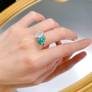 Close-up of a dual-stone ring with pear-cut green and rectangular clear gemstones