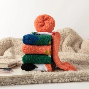 Set of five thick coral fleece winter socks in vibrant colors on soft beige blanket