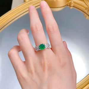 Gros plan détaillé d'une bague émeraude avec pierres latérales marquise portée au doigt