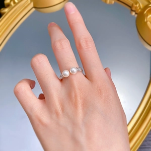Detailed view of silver open ring with dual white pearls worn on index finger