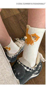 Detail of white cotton sock featuring a cute orange cartoon cat with a 3D pom-pom tail