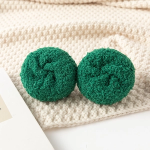 Detailed view of textured dark green plush pom poms on a soft beige knitted blanket