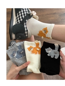 Detail of funny 3D cat tail pom poms on gray, white, and black cotton crew socks