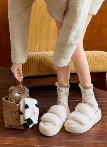 Close-up of cozy coral fleece socks with bear and cow patterns and white plush slippers