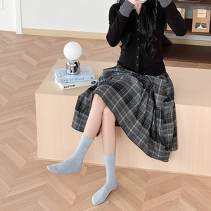 Détail de chaussettes rayées bleu clair portées avec une jupe plissée à carreaux gris