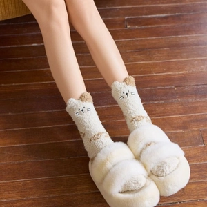 Close-up of cozy coral fleece socks with cat embroidery on a dark wooden floor