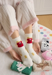 Close-up of soft coral fleece winter socks with cartoon 3D patches on warm plush carpet