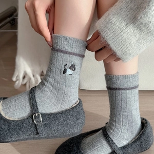 Détail de chaussettes en laine grise avec une broderie délicate de chat noir sur le côté
